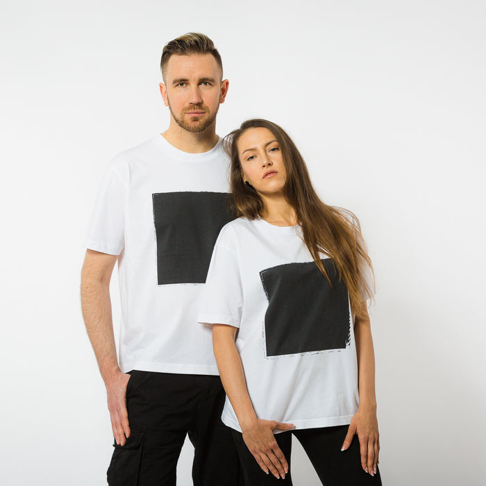 A male and female both wearing a boxy white organic cotton t-shirts with a black square print on the front