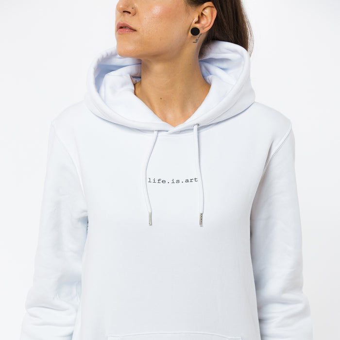 A model in a white hooded sweatshirt with a sentence ,,life. is. art" written on the chest. The hoodie is made by sustainable brand Yulunga.