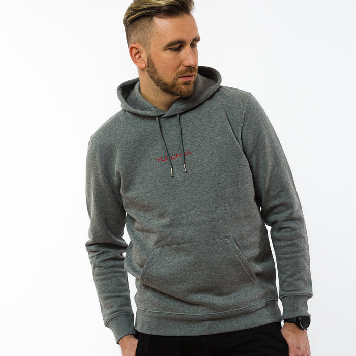 A male wearing a grey unisex hoodie made from sustainable cotton with a red embroidery of Yulunga brand logo on the front.