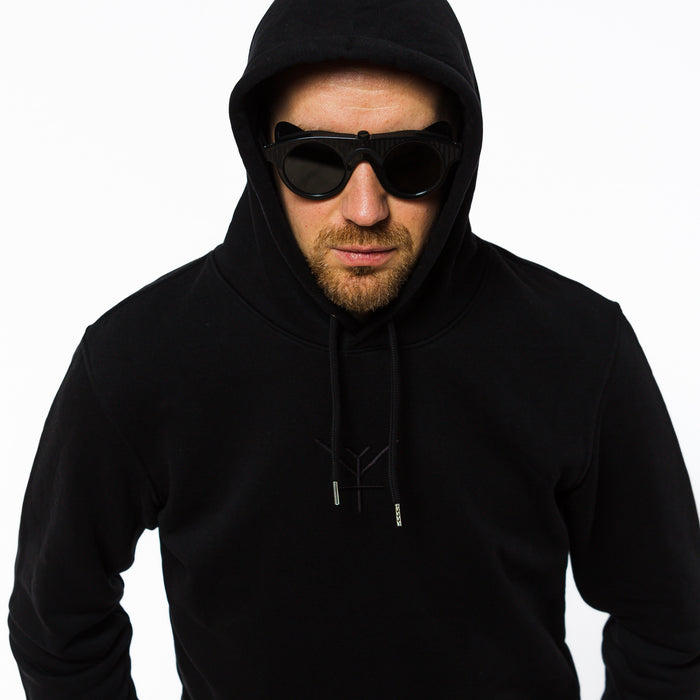 A male wearing a plain unisex black hoodie witha black Yulunga brand logo embroidery