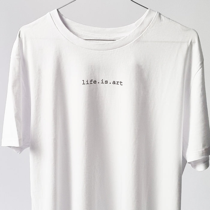 A white minimalistic design t-shirt made of organic cotton with ,,life. is. art " sentence printed in black on the chest. The t-shirt is by Yulunga, a UK sustainable brand.