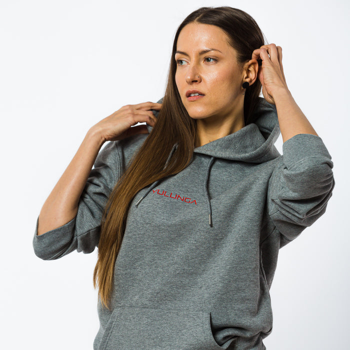 A female wearing a unisex grey hoodie with a red embroidered Yulunga brand logo on the chest