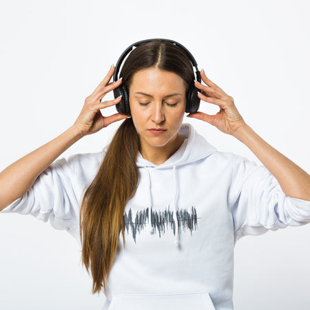 A female model wearing a minimalistic white hoodie made from eco-friendly cotton with a black print of sound waves on the chest